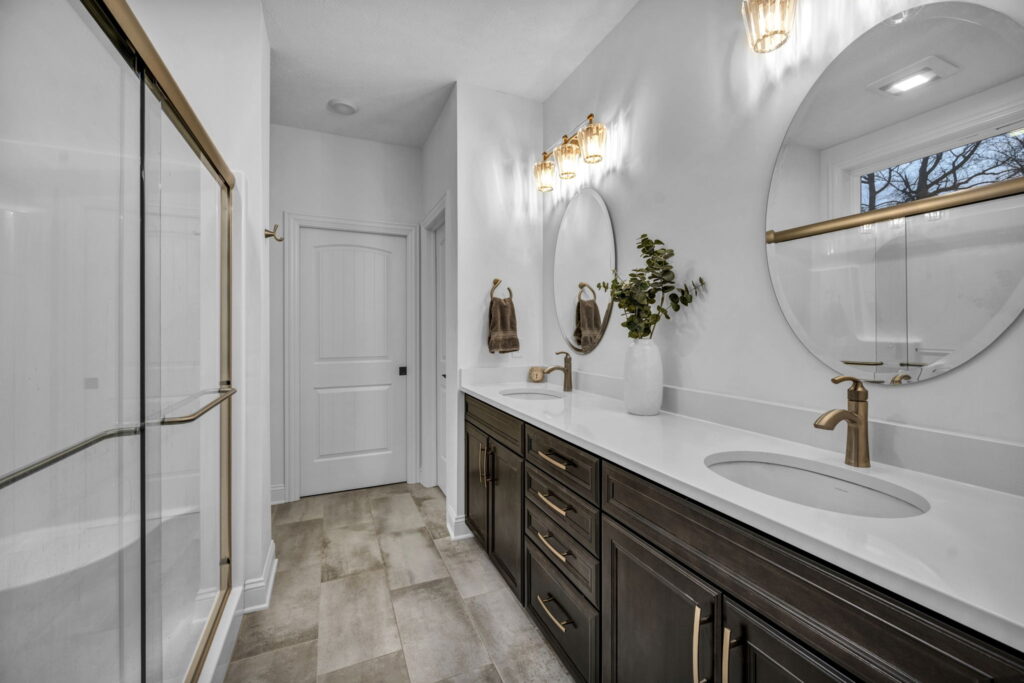 Cleveland real estate listing bathroom with modern double vanity, dark cabinetry, gold hardware, and glass shower enclosure